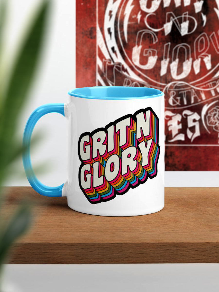 A white and blue ceramic mug with a colorful 'Grit N Glory' logo print.