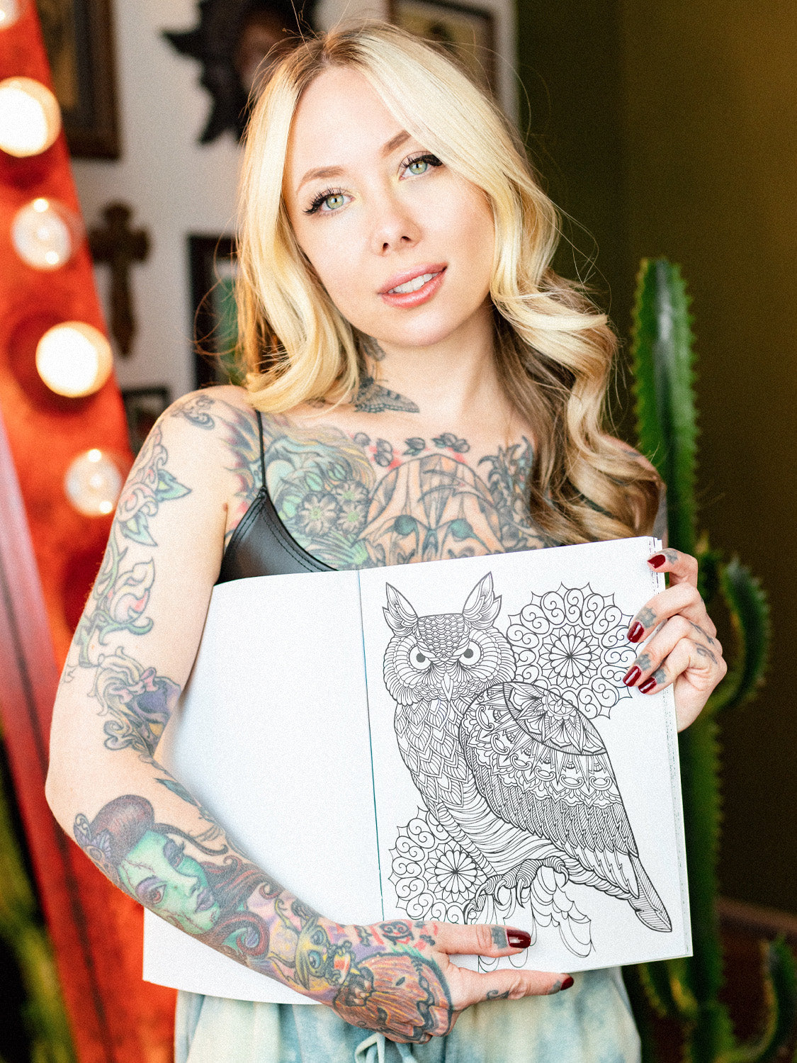 Megan Massacre holding her coloring book Marked in Ink open to a coloring page featuring a mandala style owl with ornamental background designs. Sheet is black and white. 