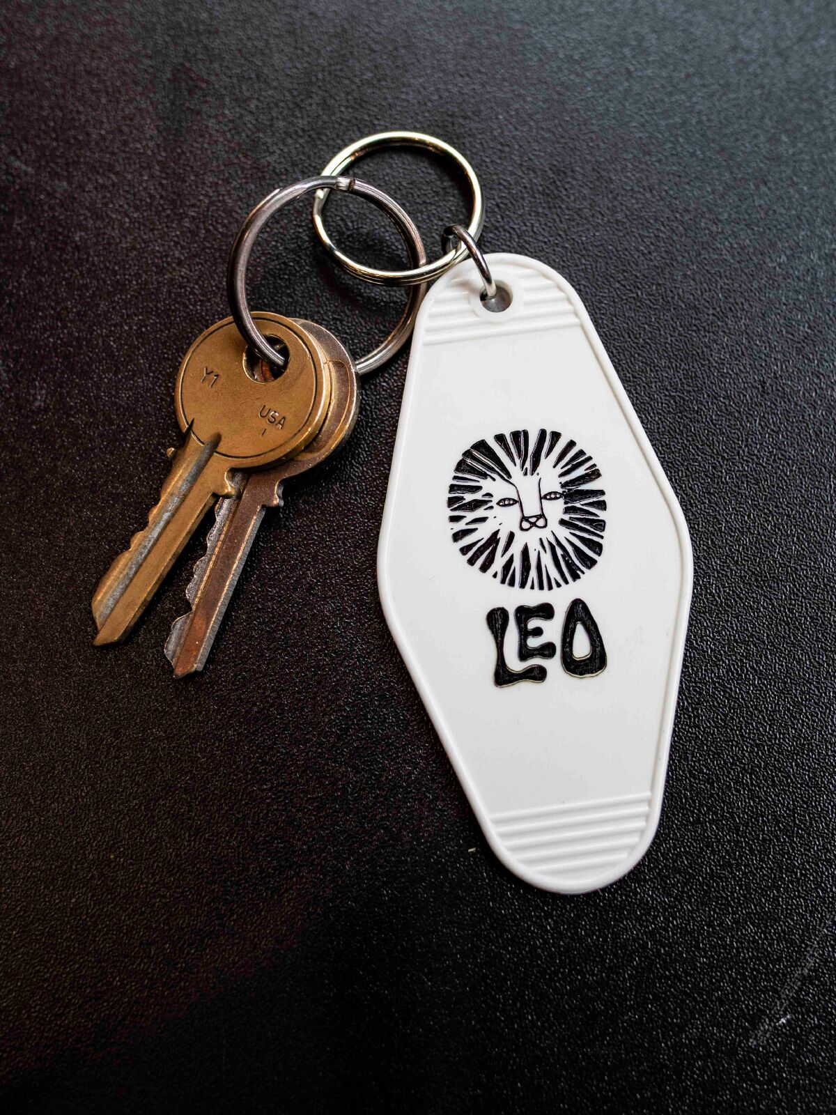 White retro motel style astrology keychain with two keys on a black solid background. 